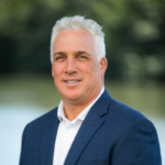 A confident middle-aged man in a blue blazer outdoors.