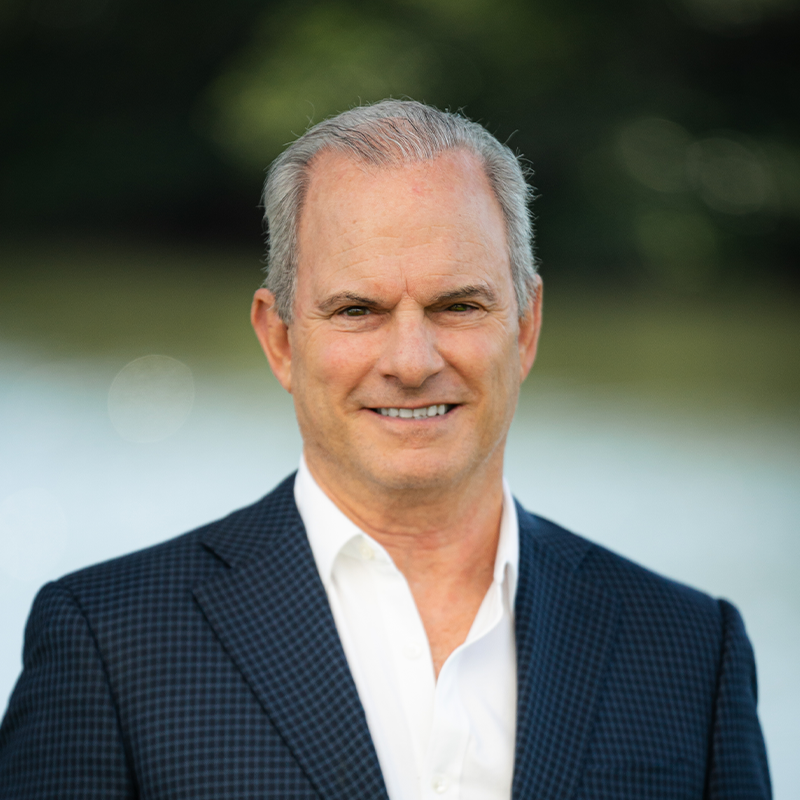 Professional man in a dark blazer smiling outdoors.