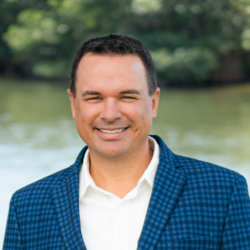Smiling man in a blue blazer outdoors by water.
